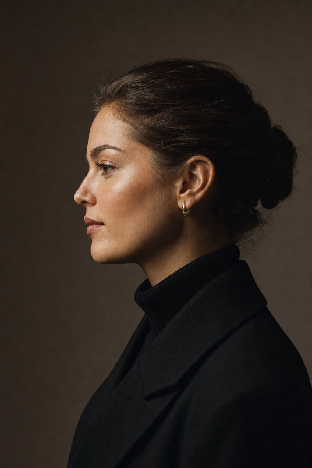 Elegant profile of a young woman against deep warm shadow. Illustrative image — not a patient.