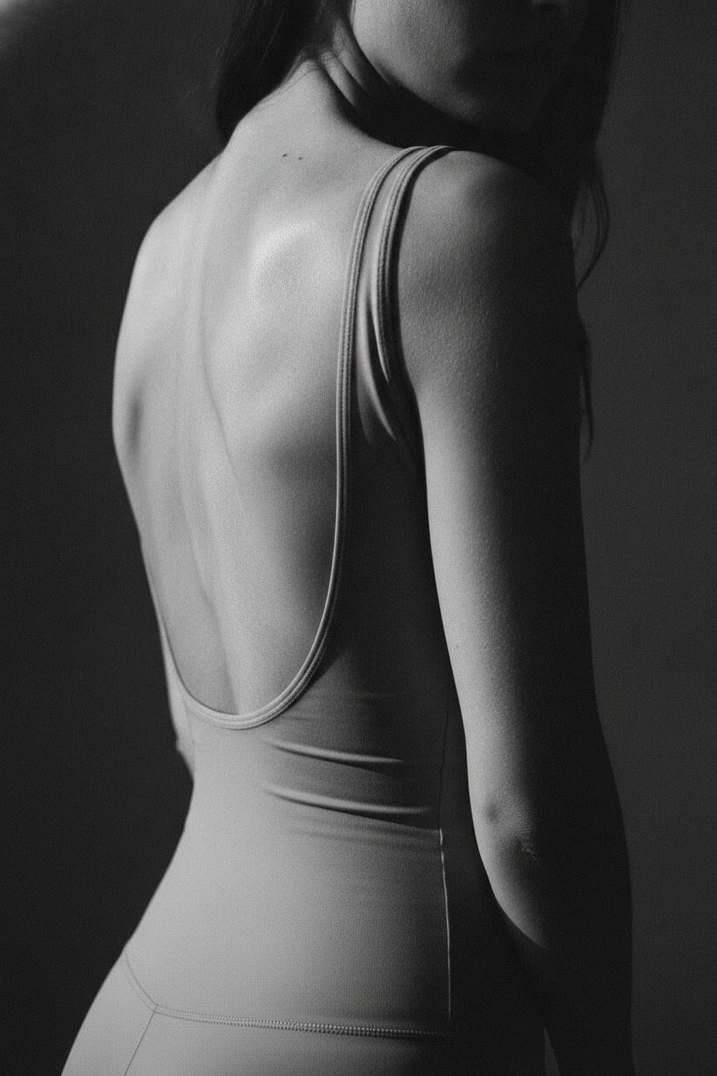 Black-and-white form study of a back and shoulder in raking light, face out of frame. Illustrative image — not a patient.