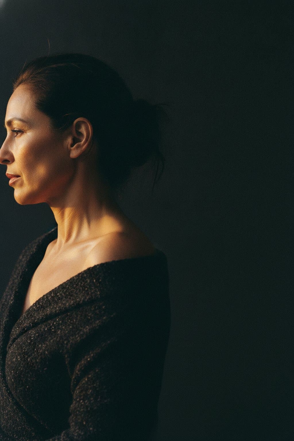 Sculptural crop of a draped shoulder and collarbone in warm rim light. Illustrative image — not a patient.